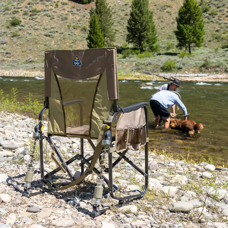 Tan Adjustable Rocker chair sits near a river as a person helps their dog in the water.