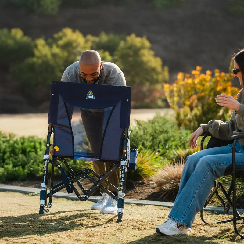 Smiling man sets up an Adjustable Rocker chair while a woman watches from her seat outdoors.