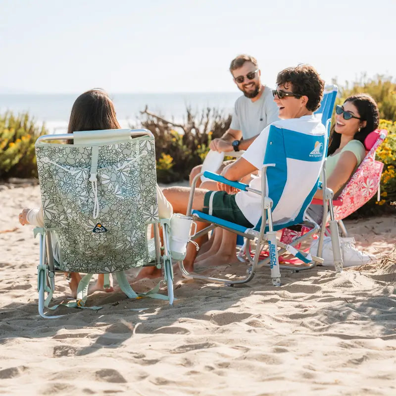 Friends laughing and lounging in Saybrook Blue Beach Rockers and other chairs on a sandy beach.
