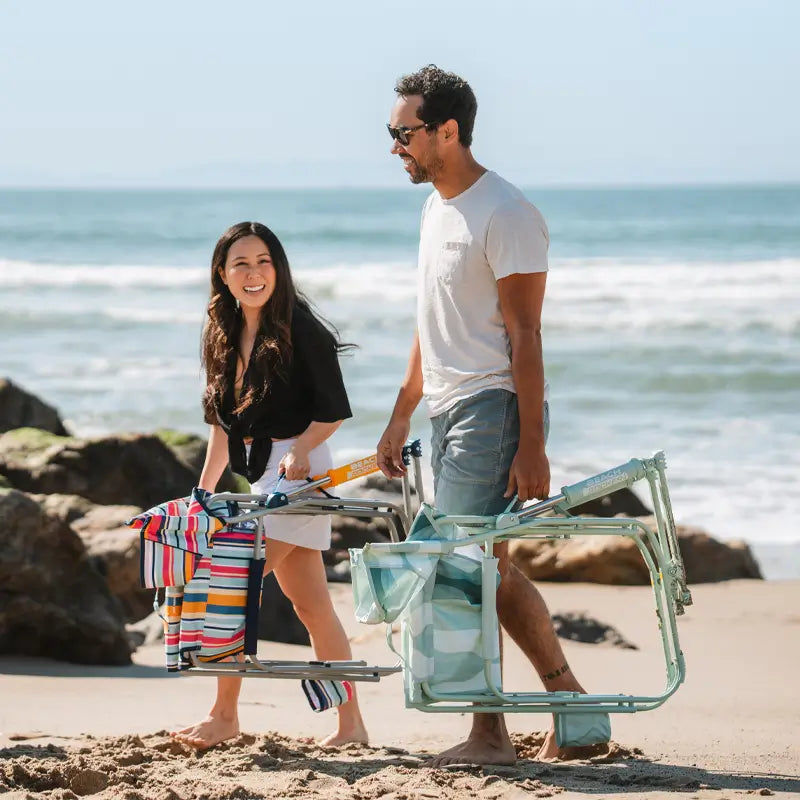 Couple walking along the beach carrying folded Beach Rocker Chairs.