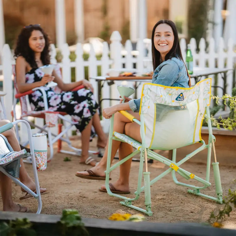 Group of women relax outdoors, one smiling in a daisy-patterned Freestyle Rocker.
