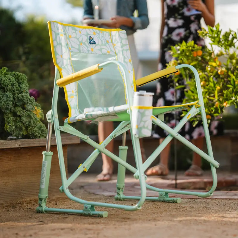 Close-up of an empty floral Freestyle Rocker chair on a garden path near greenery.