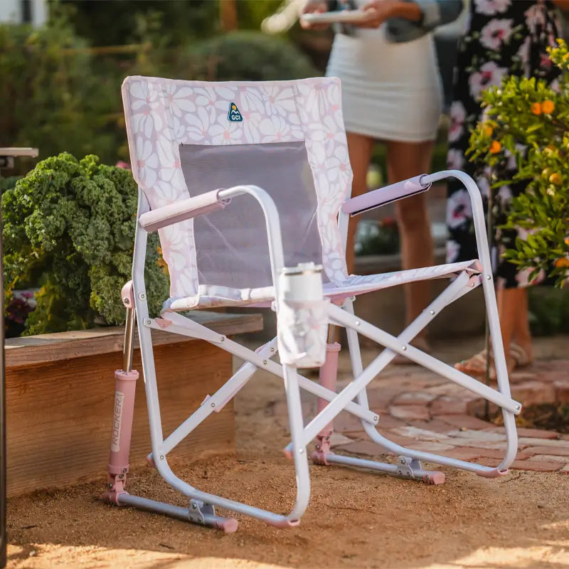 Pink and white floral Freestyle Rocker with mesh back and drink holder sits on a garden path.