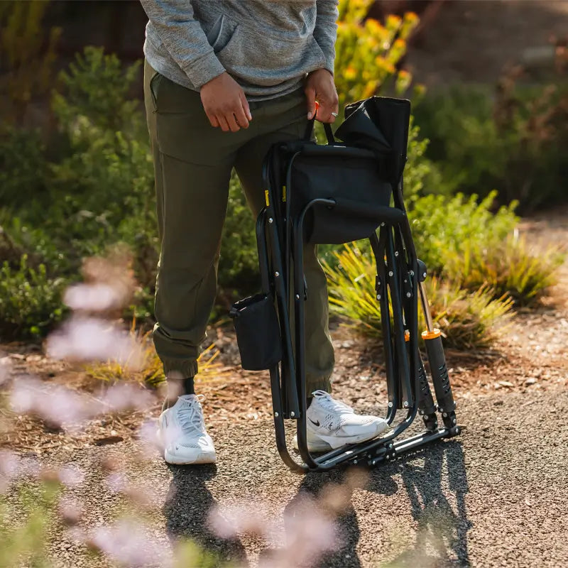 Man holding a folded Black Freestyle Rocker Elite chair by the handle.