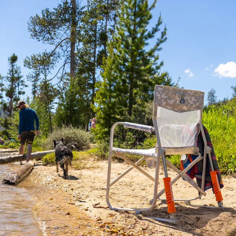 Snow Camo Freestyle Rocker Elite chair sits empty on a lakeshore with a towel draped over the side.