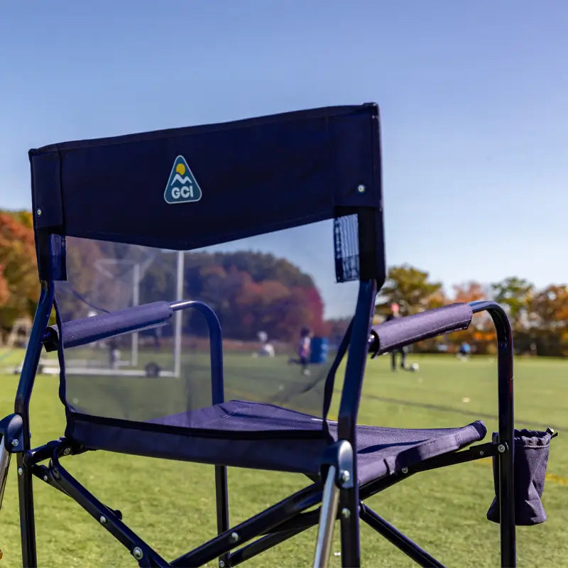 Close-up of a Rich Blue Freestyle Rocker Elite chair on a grassy field, facing a soccer game in the distance.
