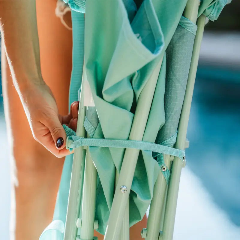 Close-up of a hand securing the strap on a folded pastel green leaf Kickback Rocker chair.