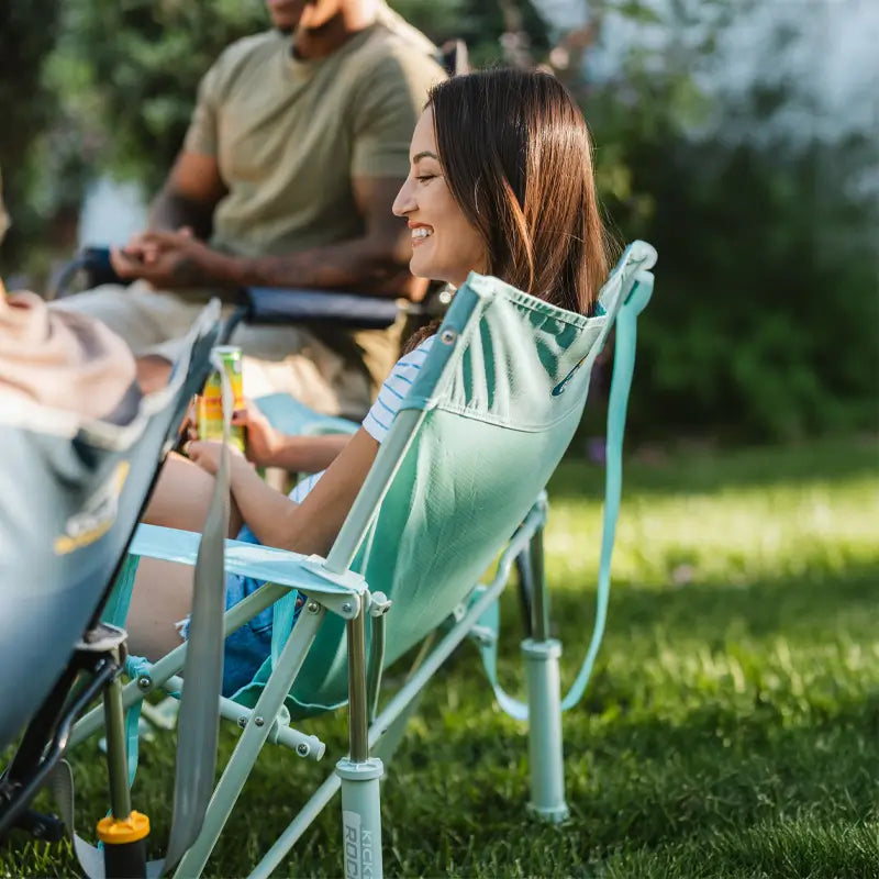 Woman relaxes in a pastel green leaf Kickback Rocker on a sunny lawn with friends.