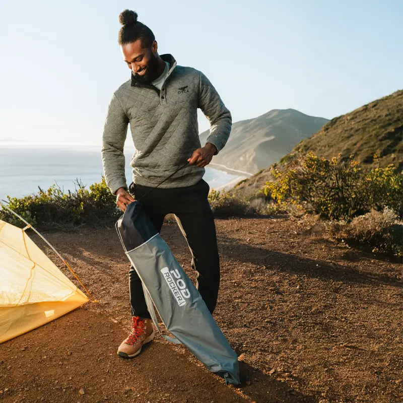 Man unpacks the indigo Pod Rocker chair at a scenic coastal campsite. all-groups