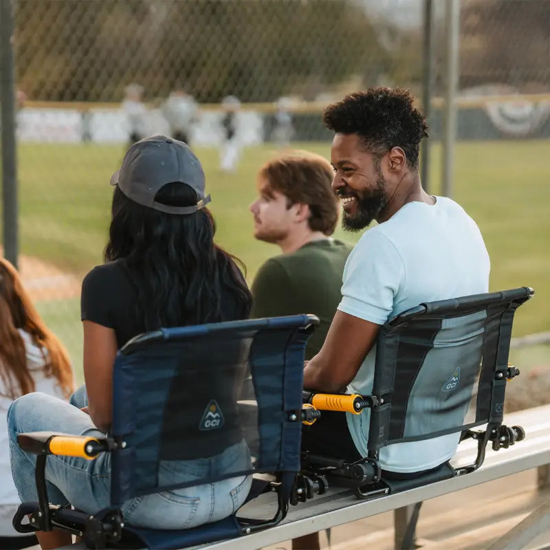 Two people sitting on bleachers in Stadium Rock-Cliners, watching a baseball game.
