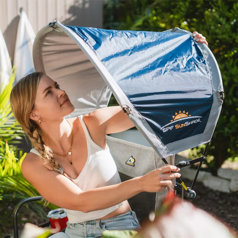 Woman smiling while securing an Indigo SunShade Accessory above her outdoor chair.