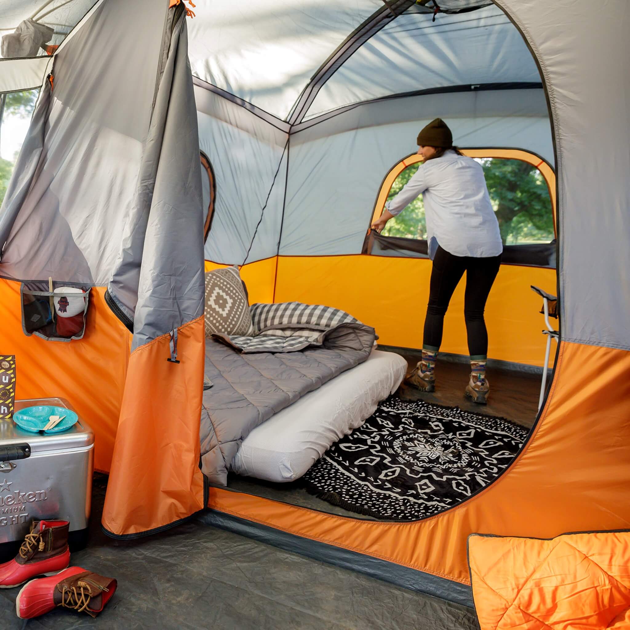 CORE 11 person straight wall cabin tent with screen room in orange and gray set up at a campsite with camper rolling down window inside of tent.