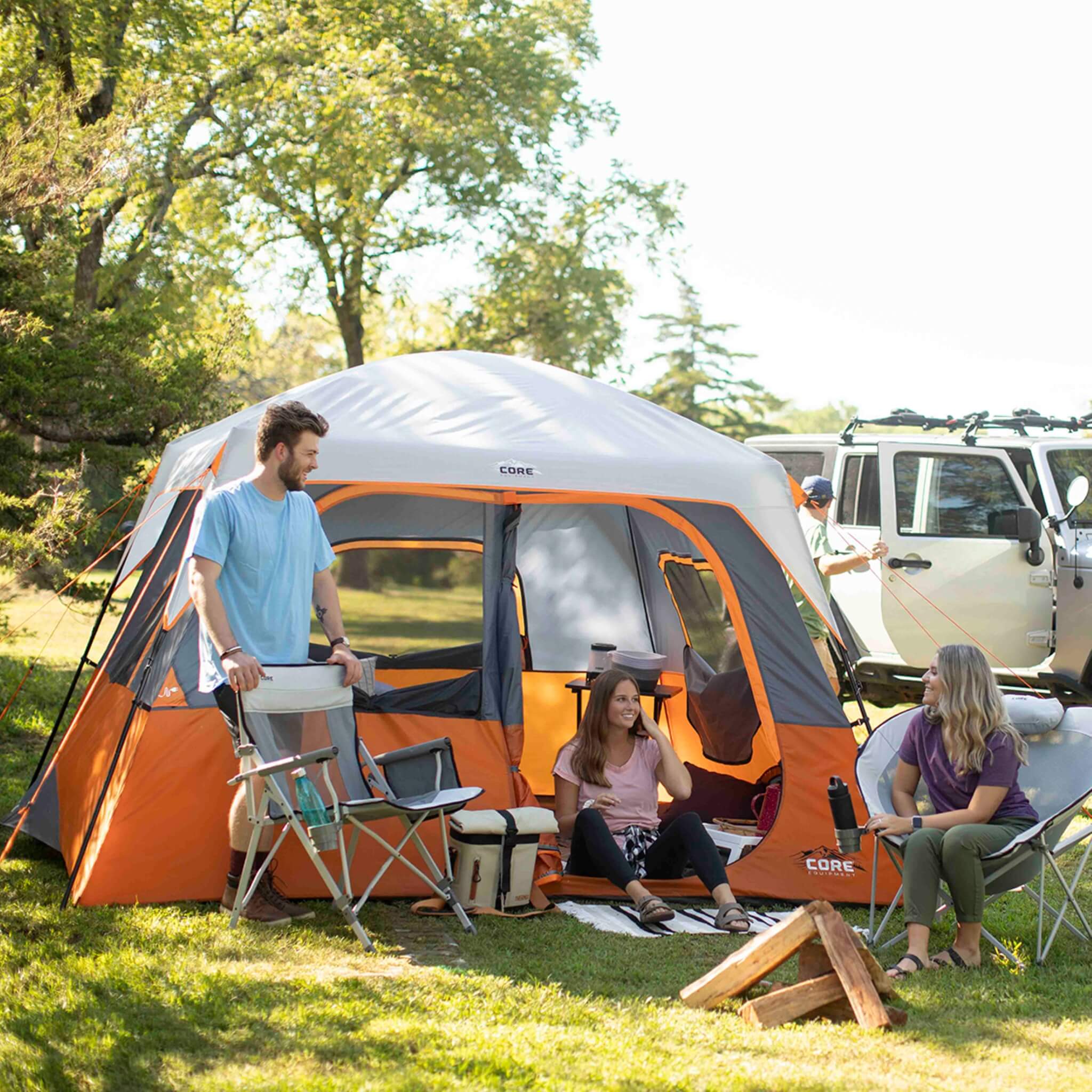 Friends hanging out next to a CORE 6 person straight wall cabin tent in orange and gray.