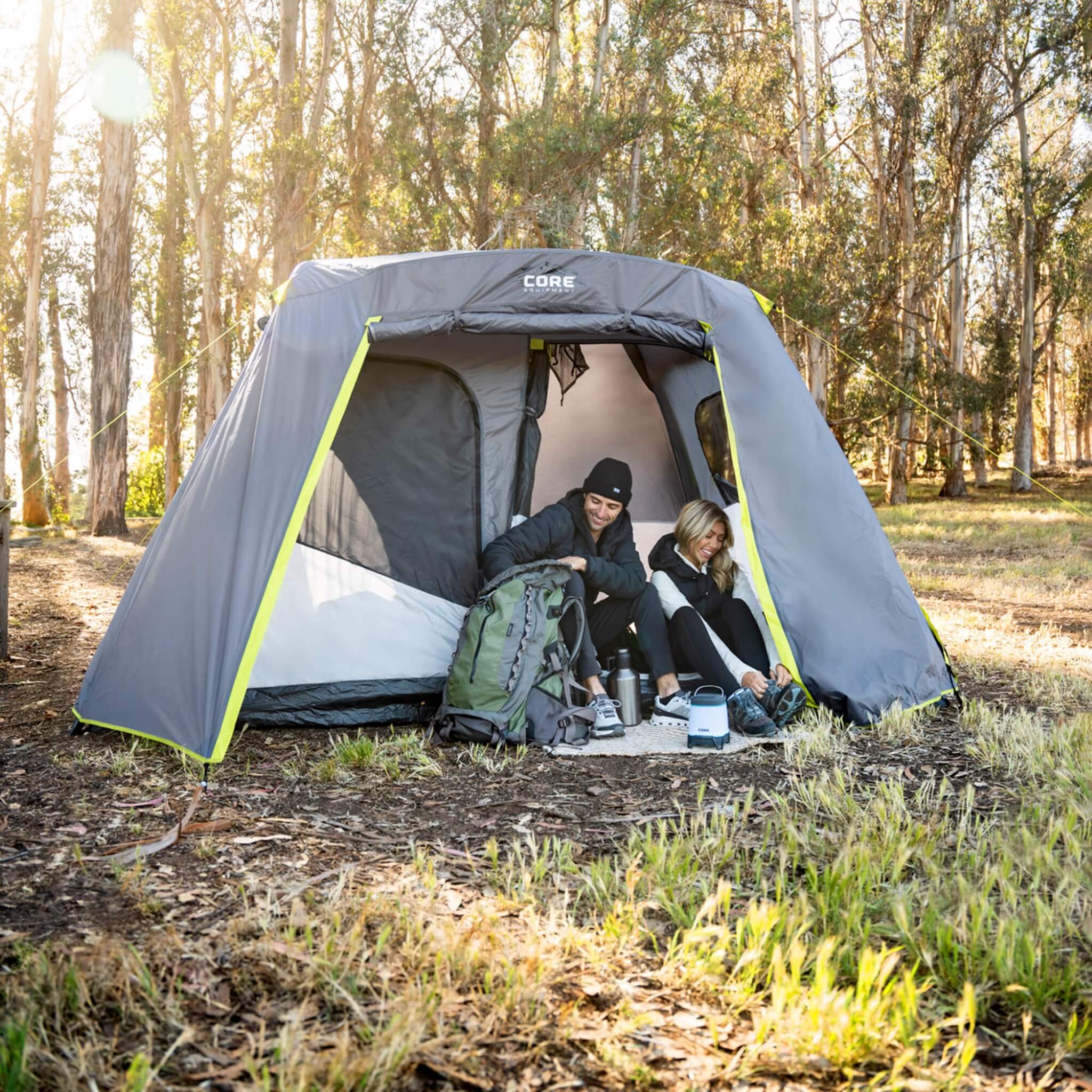 Campers sitting in CORE 6 person instant cabin tent with full rainfly at wooded campsite, showing quick setup and roomy design.