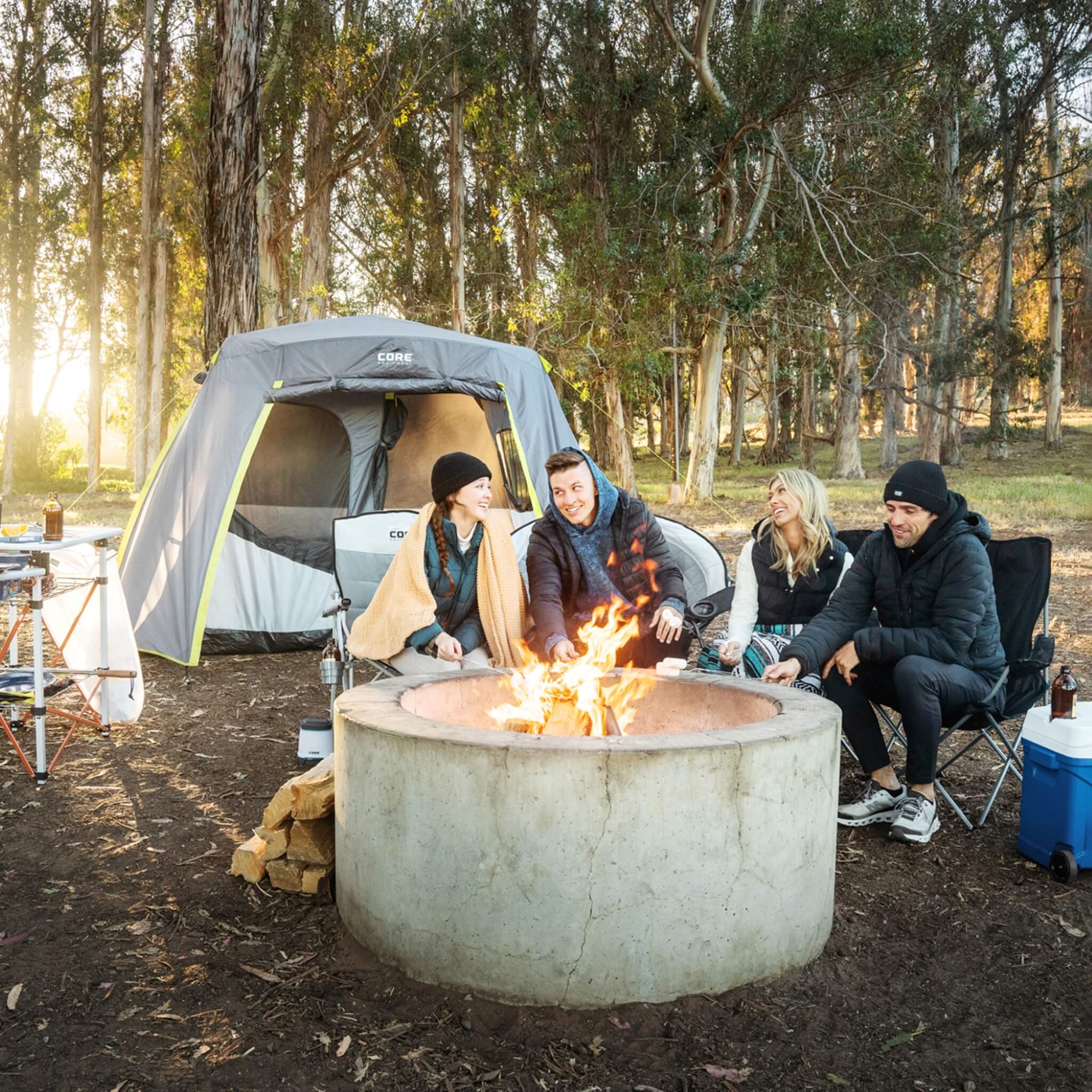 Friends gathered around campfire with CORE 6 person instant cabin tent in background, highlighting easy setup and spacious size.