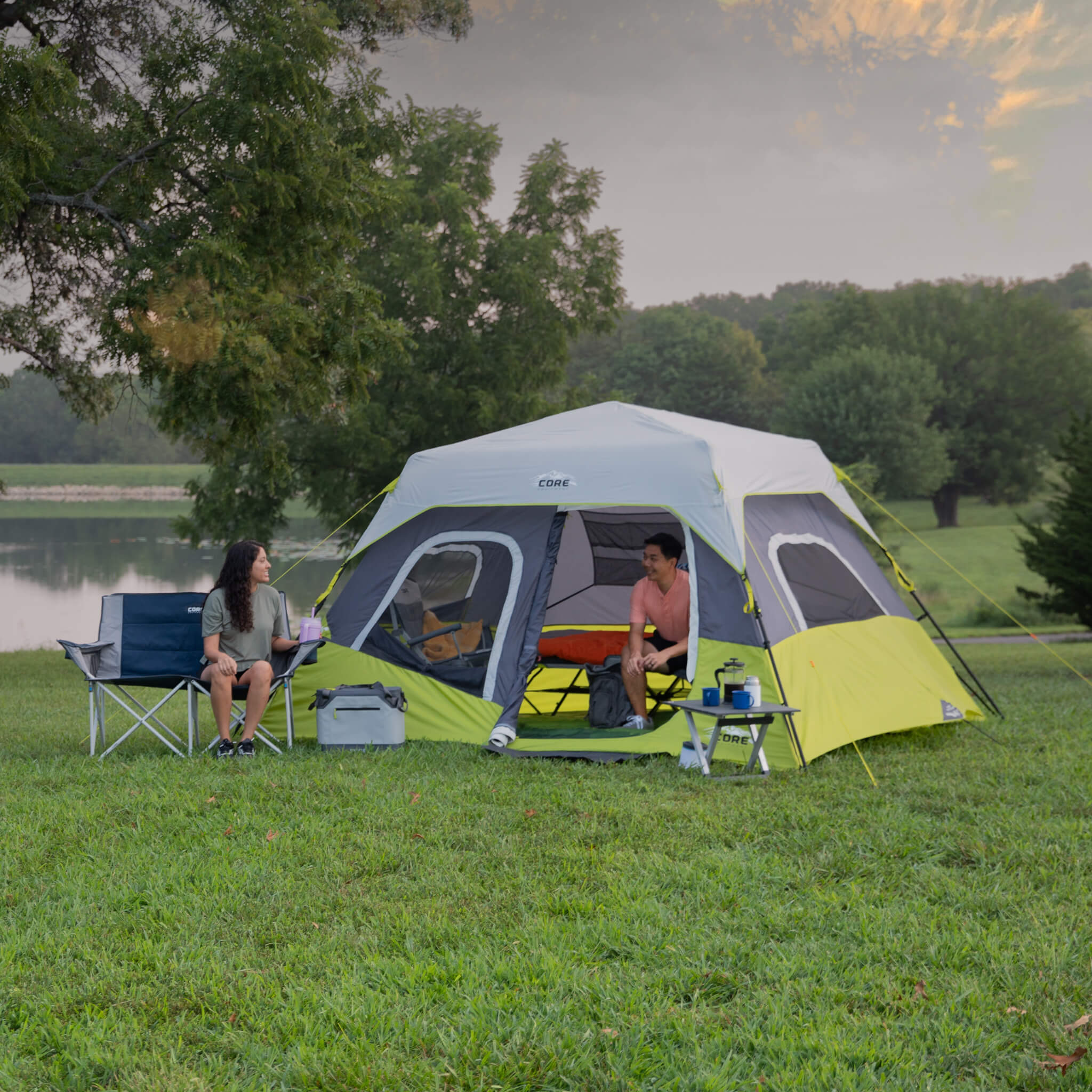Campers relaxing beside the CORE 6 person instant cabin tent in dark gray and green, designed for fast setup and reliable weather protection.