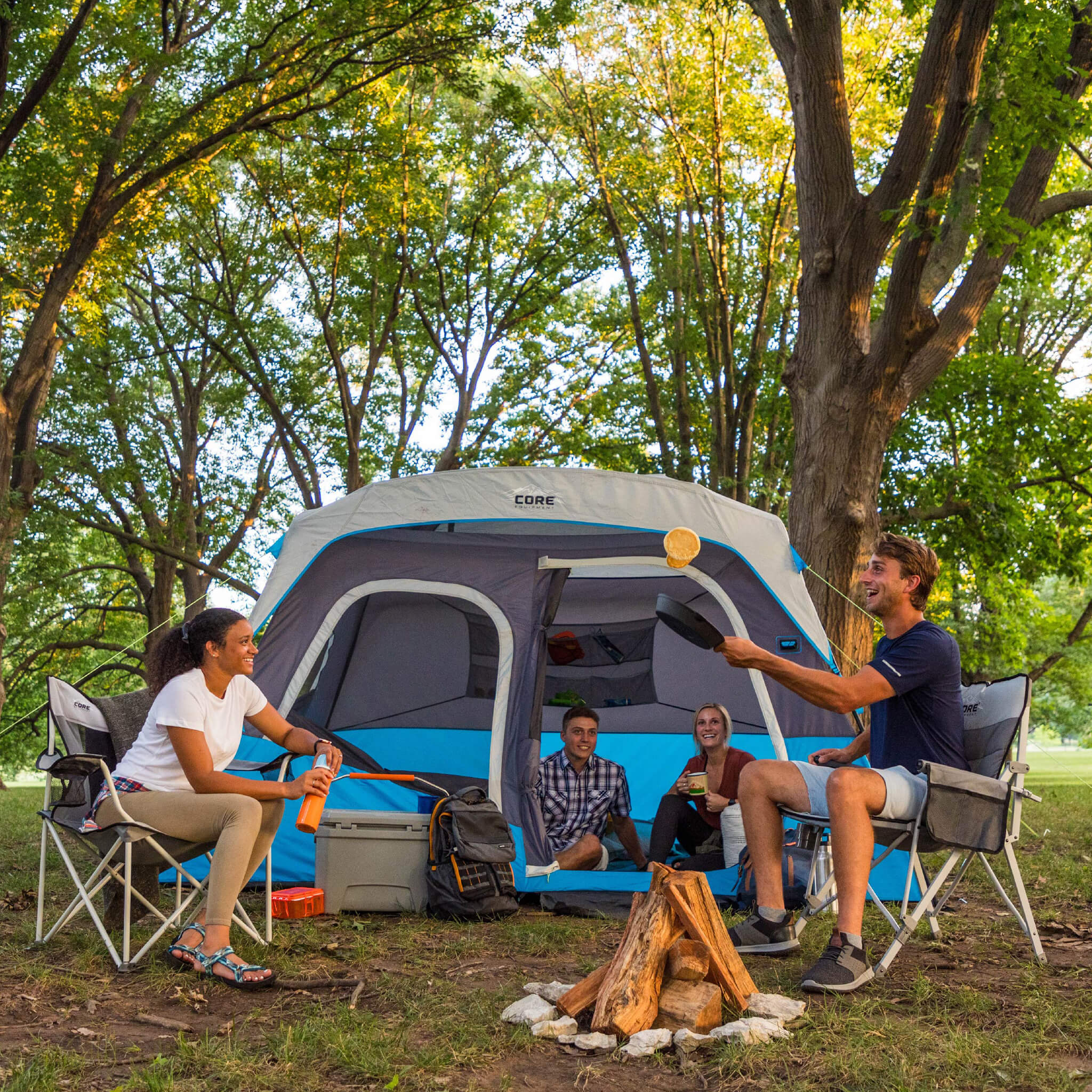 Friends enjoying time inside and outside the CORE 6 lighted person instant cabin tent in blue and gray, offering durable weather protection and comfort.