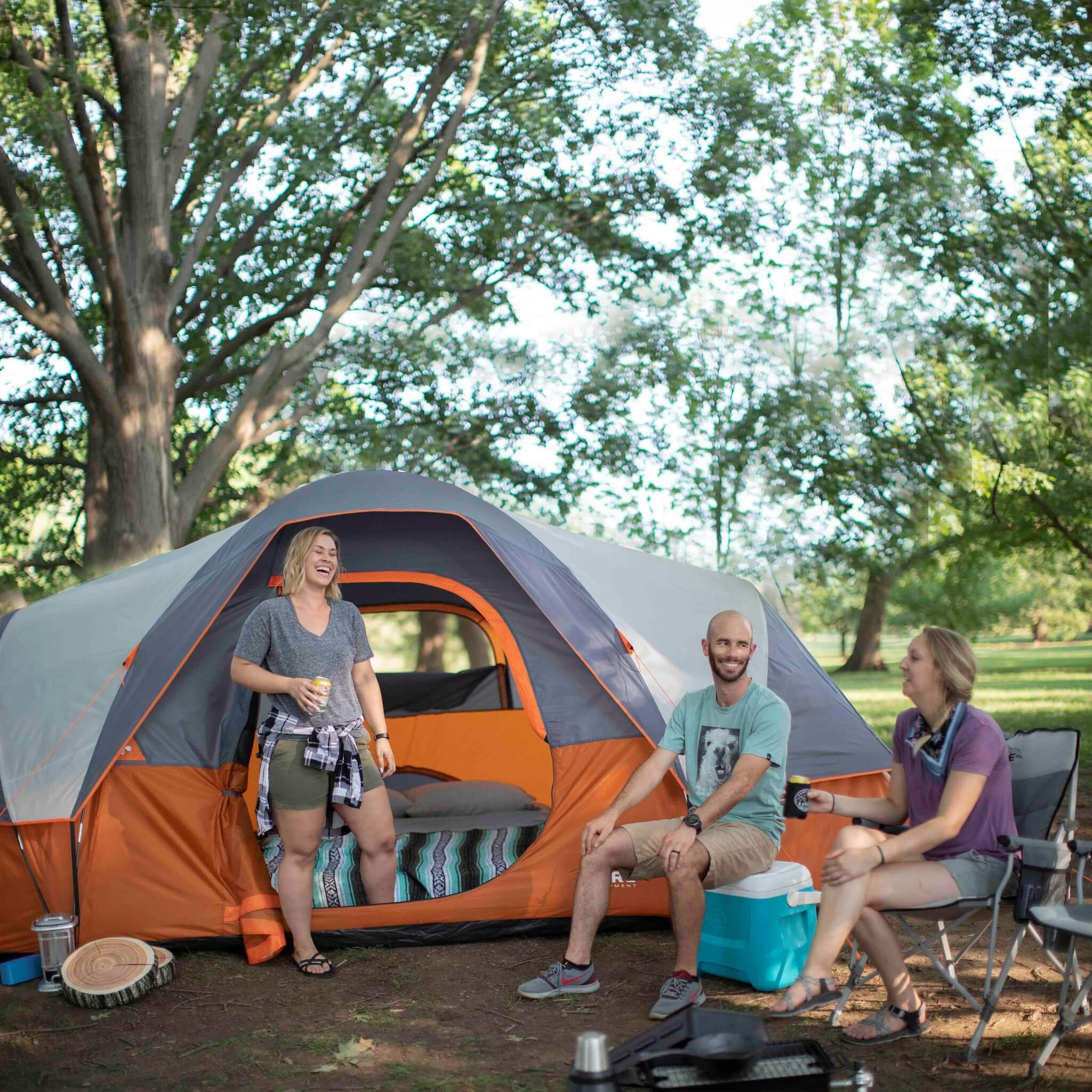 CORE 9 person extended dome tent in orange and gray shown at a campsite with campers sitting outside under trees.