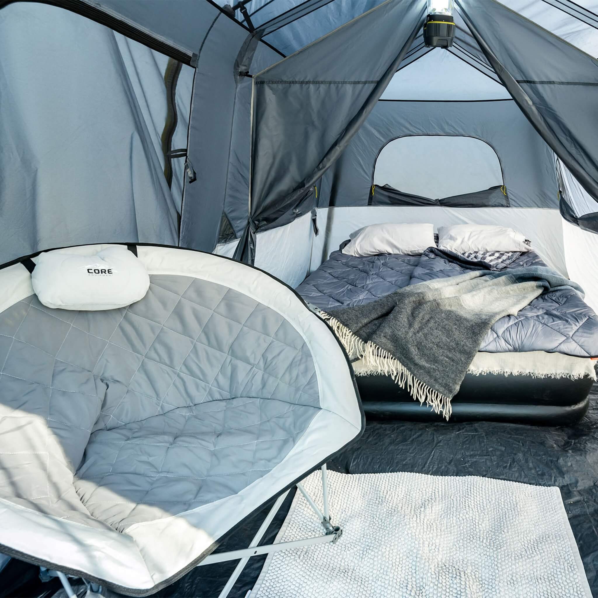 Interior of CORE 9 person instant cabin tent with full rainfly shown with air mattress, blankets, and CORE camp chair, highlighting spacious living area.