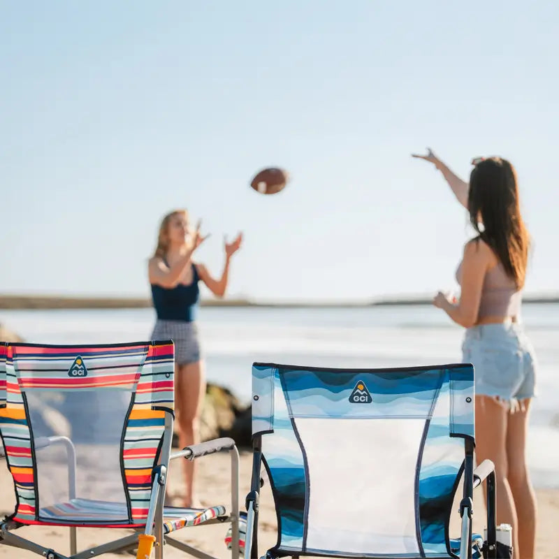 Two Beach Rocker Chairs side by side on the sand, with two people playing with a football in the background.