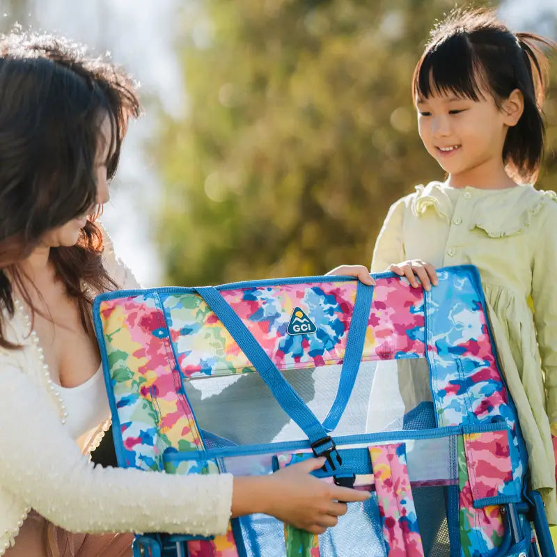 Adult and child smiling while examining the folded tie dye Everywhere Chair 2 outdoors.