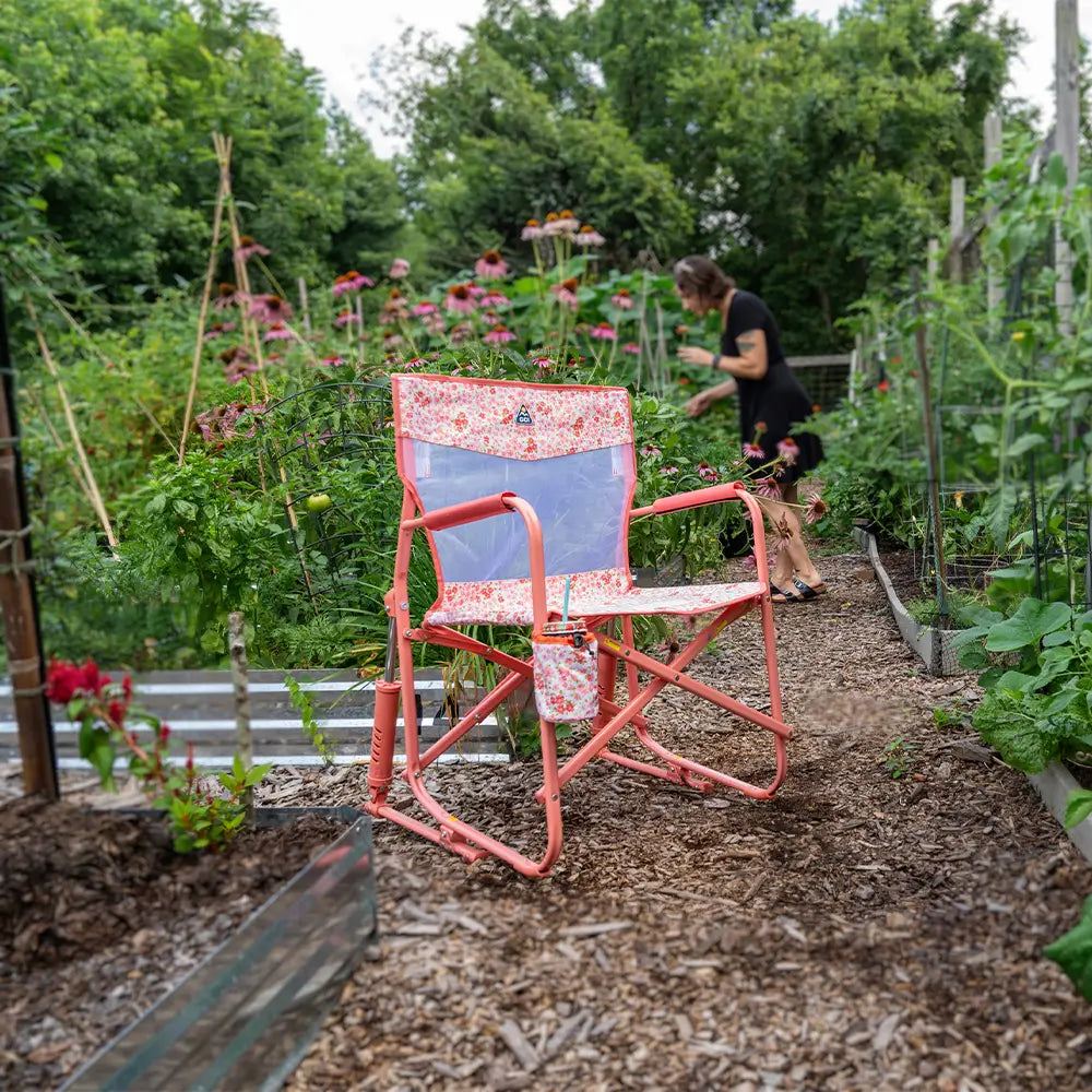 A pink sundress freestyle rocker elite chair surrounded by a garden setting.