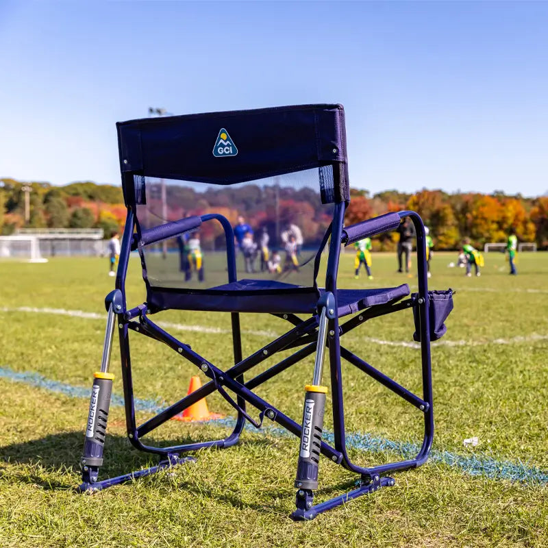 Rich Blue Freestyle Rocker Elite chair positioned on a soccer field sideline with kids playing in the background.
