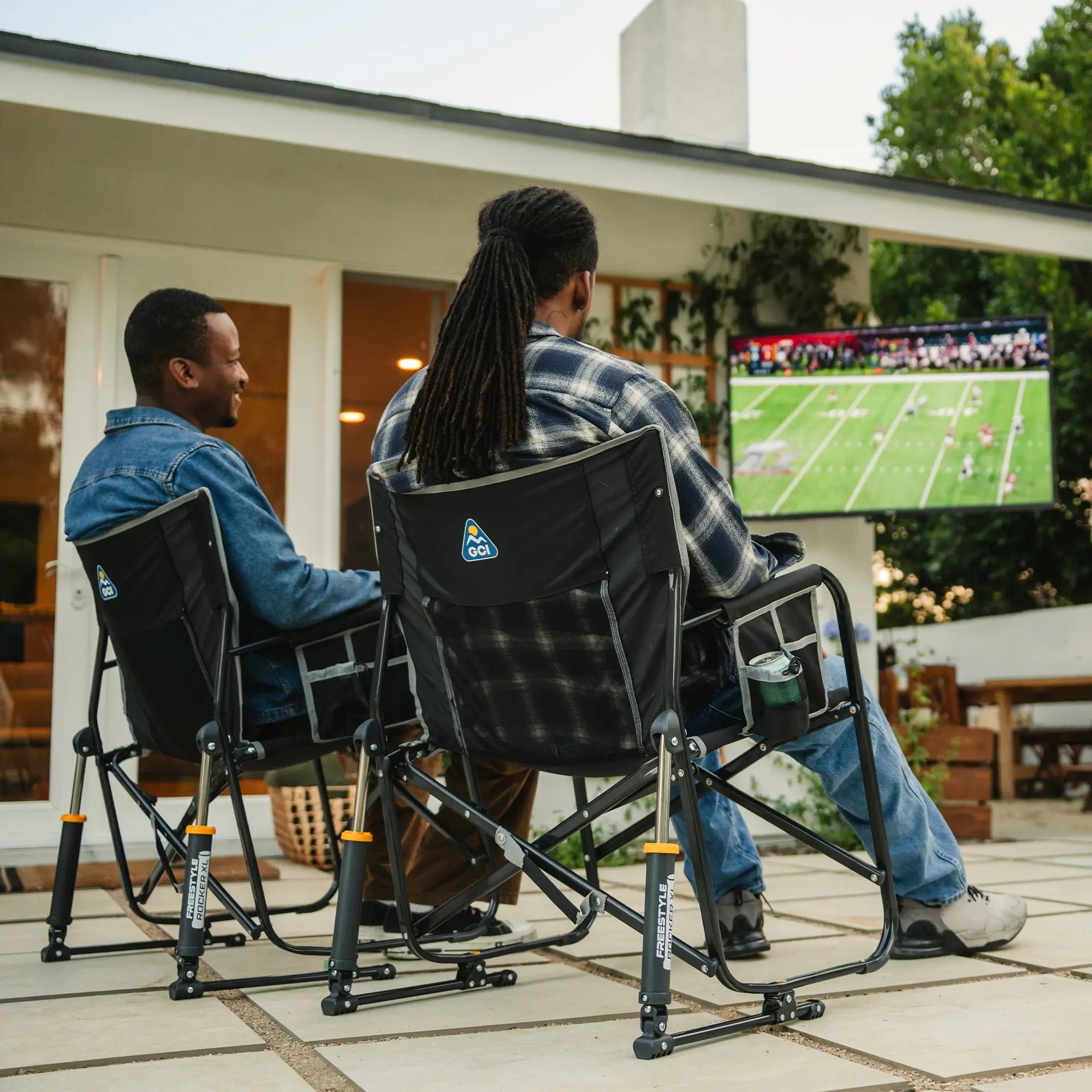 Two men sitting in black freestyle rocker xl chairs watching a football game on television. 