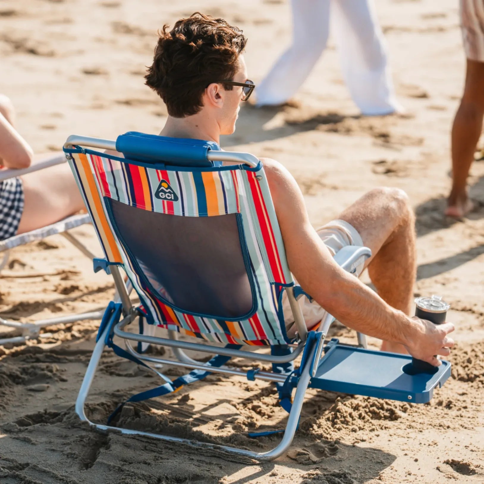 A man sitting in the big surf with slide table putting his drink onto the side table while sitting at the beach.