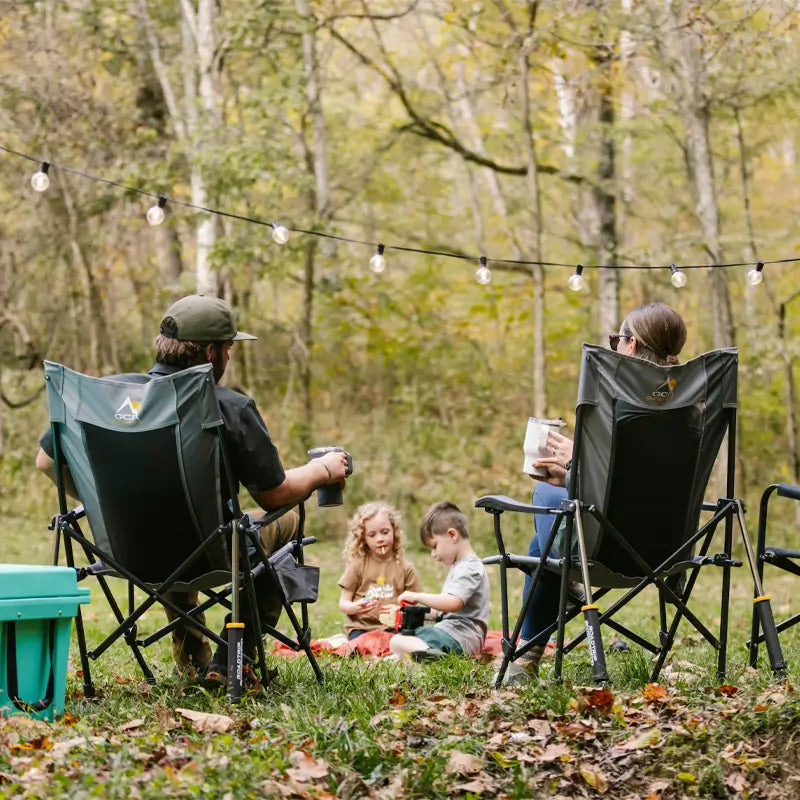 Family relaxes at a wooded campsite in mercury gray Roadtrip Rocker chairs.