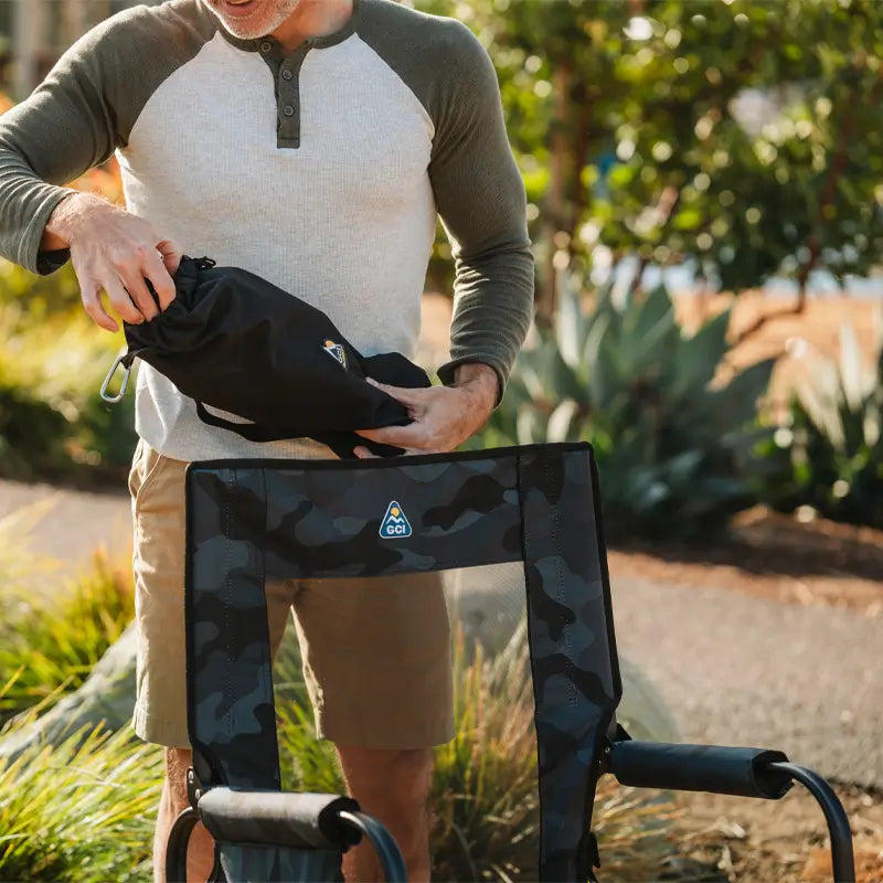 Man unpacks black sunshade accessory next to a camo GCI outdoor chair.
