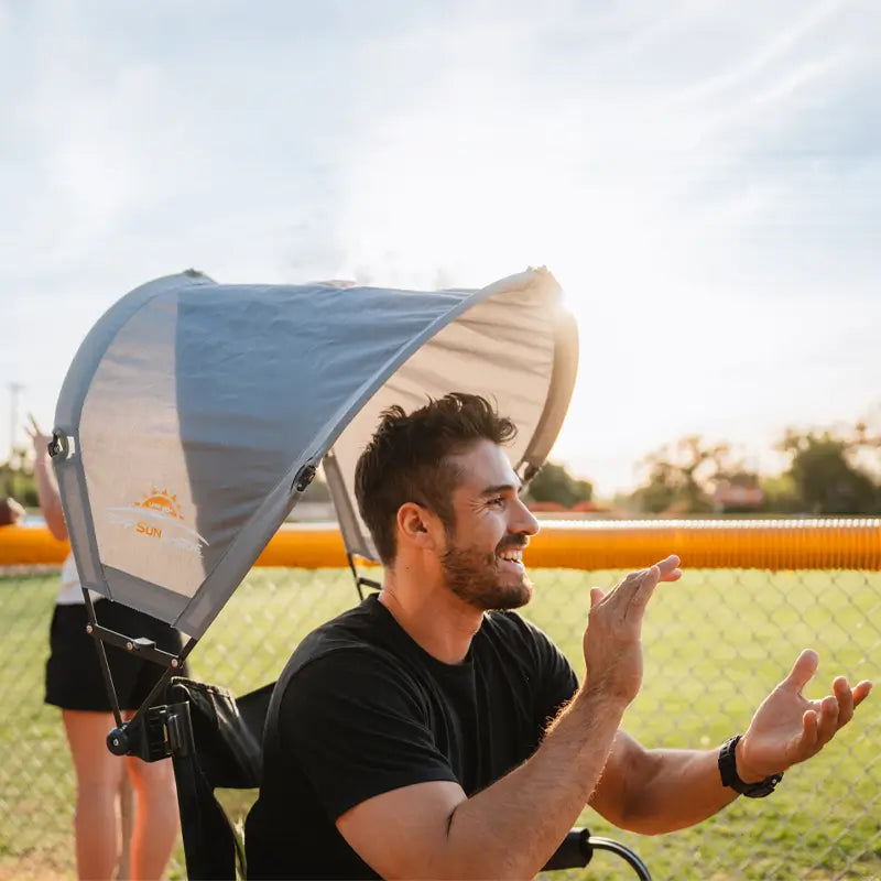 Man smiles and claps under a mercury sunshade accessory at a sunny sporting event.