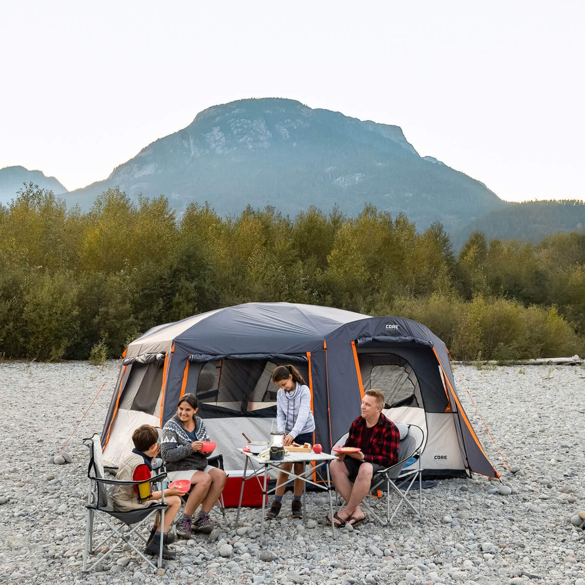 Family gathered outside CORE 10 person cabin tent with full rainfly, shown set up at a campsite with mountain views.