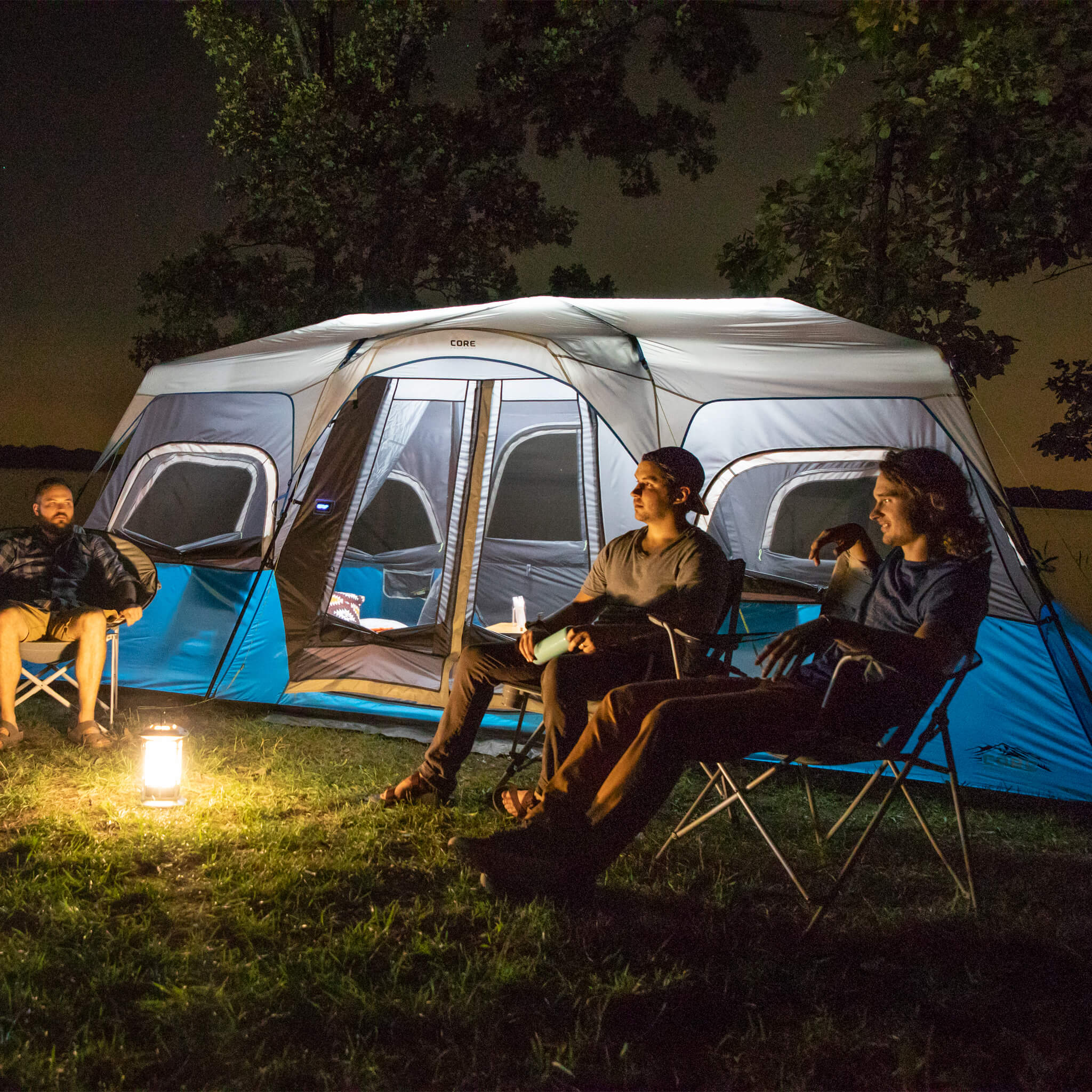 Campers relaxing beside the CORE 12 person lighted instant cabin tent in blue and gray, designed for fast setup and reliable weather protection.
