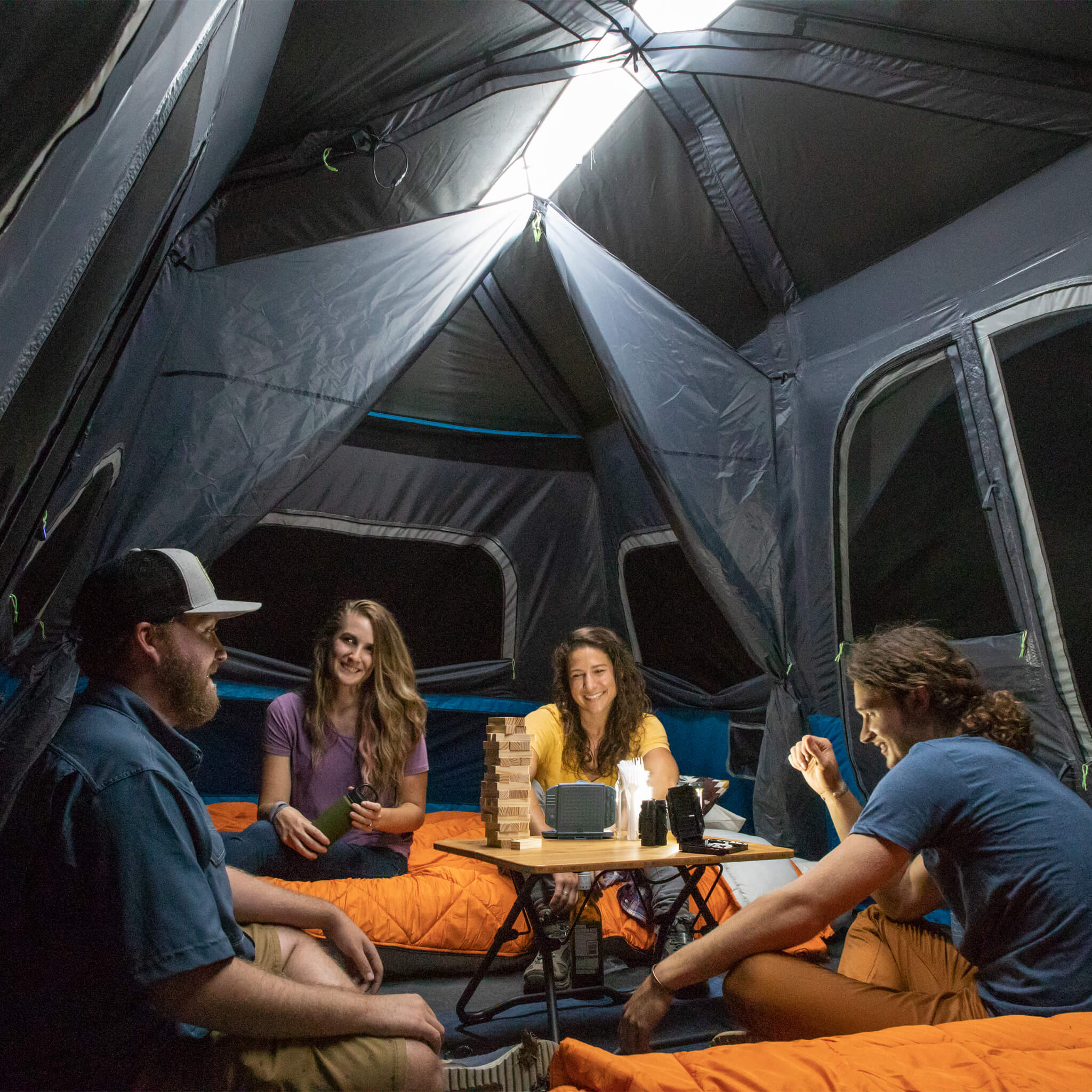 Friends at night time enjoying time inside the CORE 12 lighted person instant cabin tent in blue and gray, offering durable weather protection and comfort.