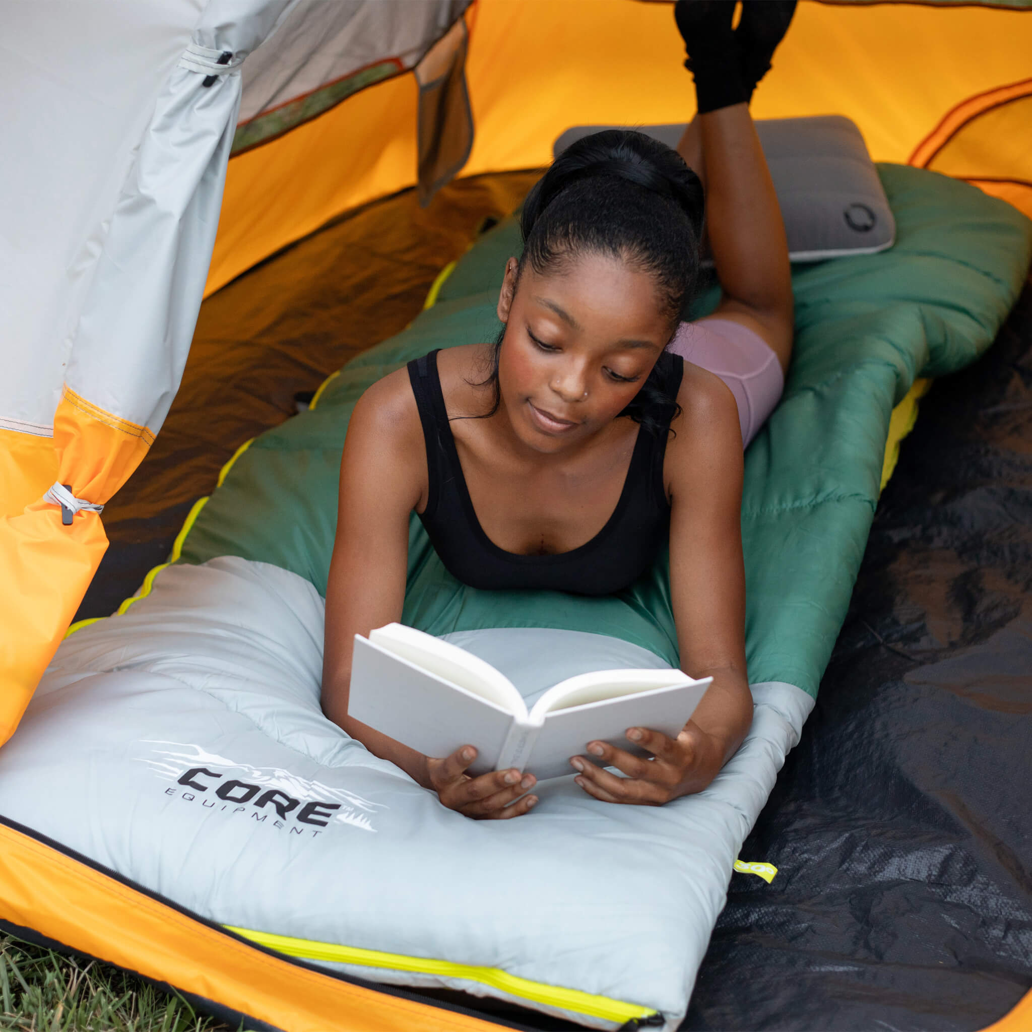 Camper reading inside a CORE 4 person dome tent, shown with sleeping bag for comfortable camping trips.