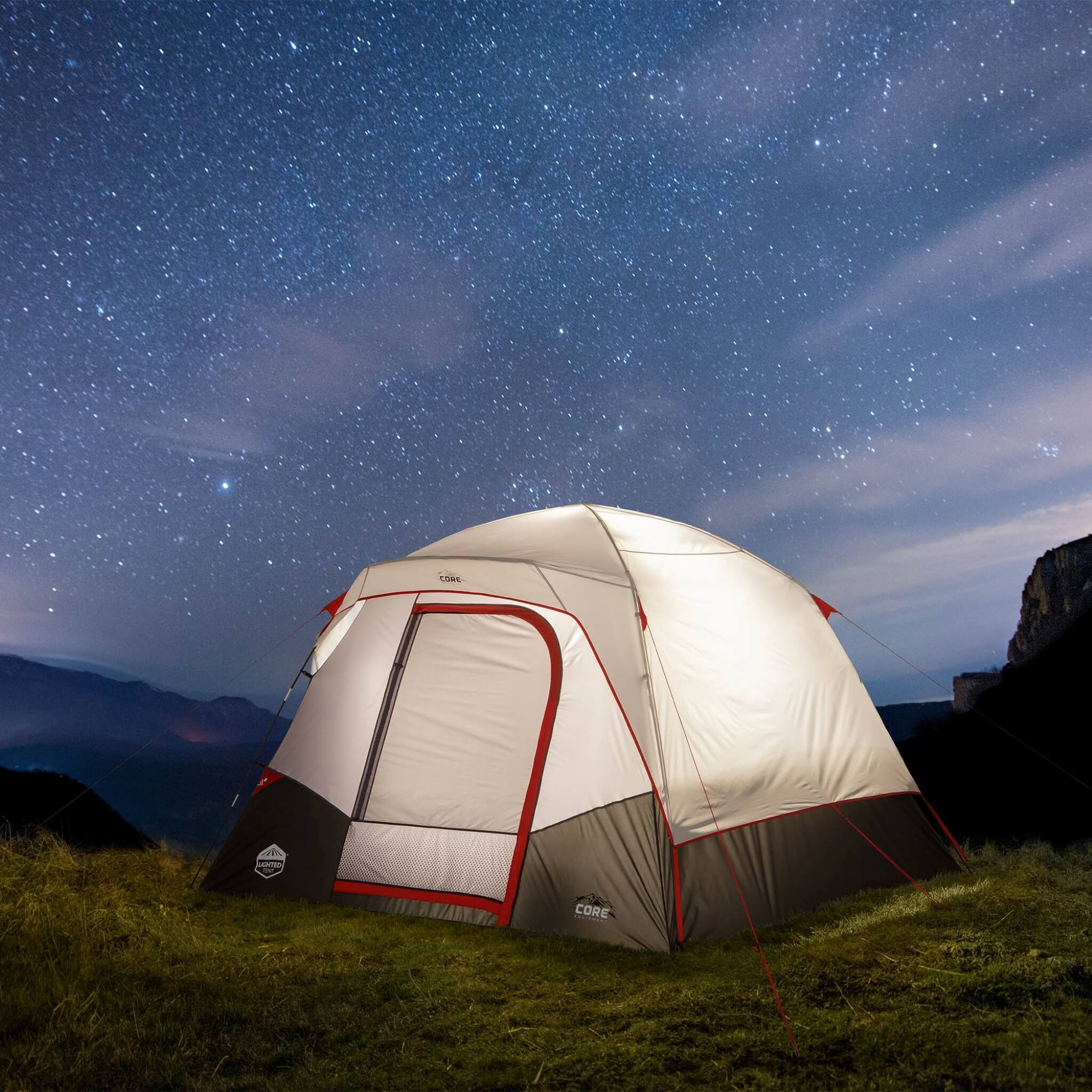 CORE 6 person lighted dome tent in gray with red accents glowing at night on a campsite, showcasing built-in interior lighting and weather protection.