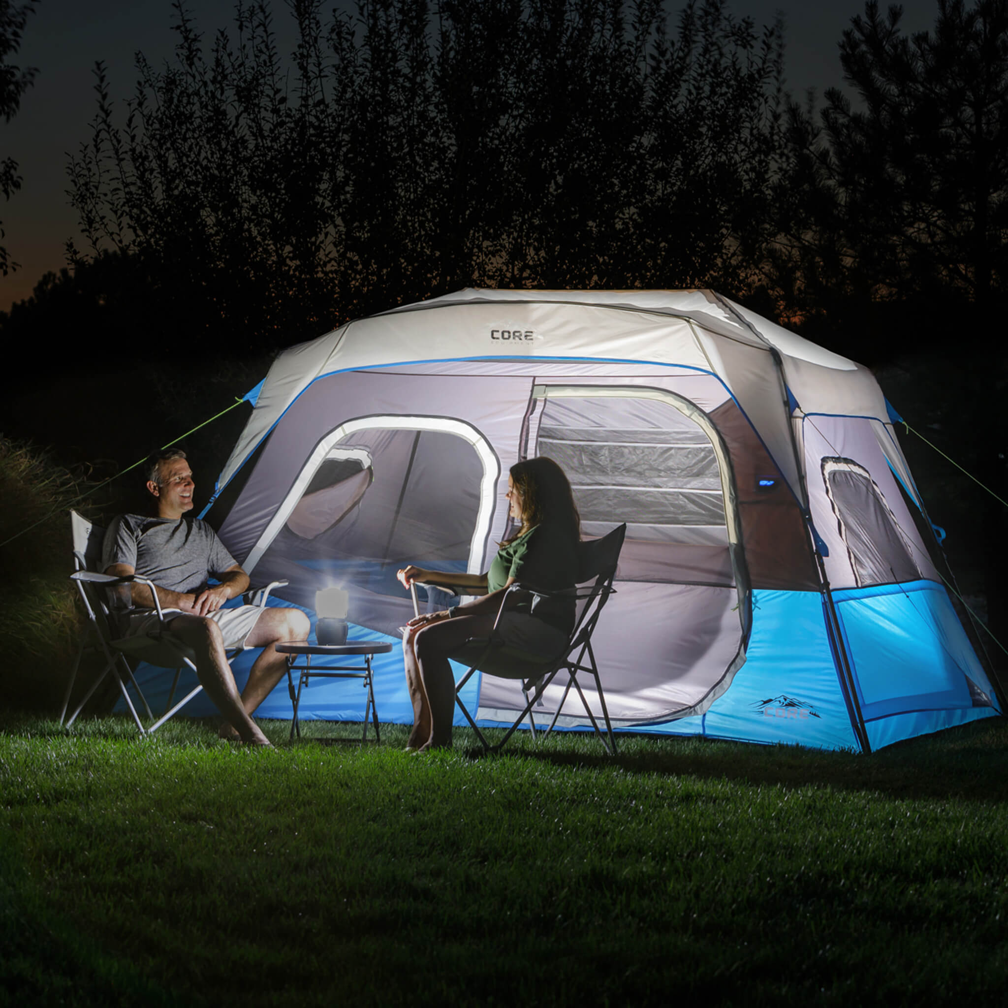 Campers relaxing beside the CORE 6 person lighted instant cabin tent in blue and gray, designed for fast setup and reliable weather protection.