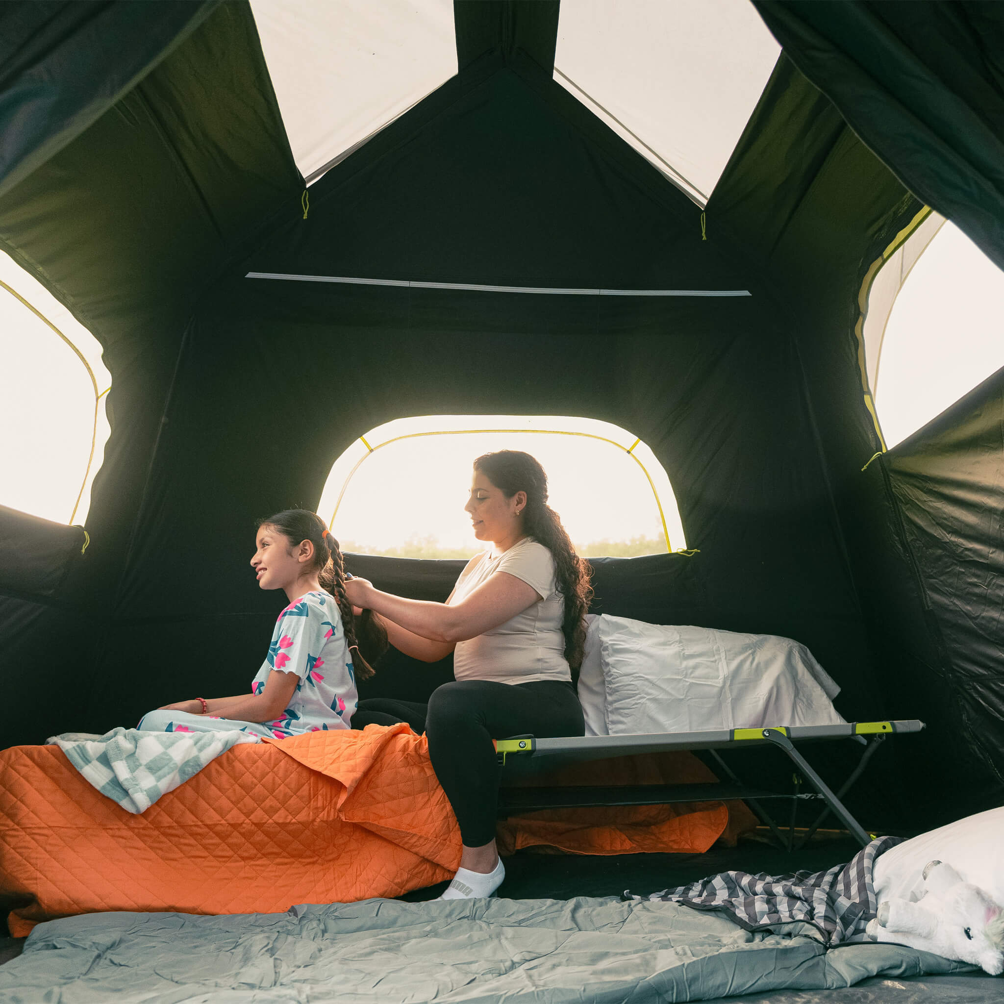 Inside CORE 9 person Blockout instant cabin tent with parent braiding child’s hair on cot, showing dark interior and roomy windows.