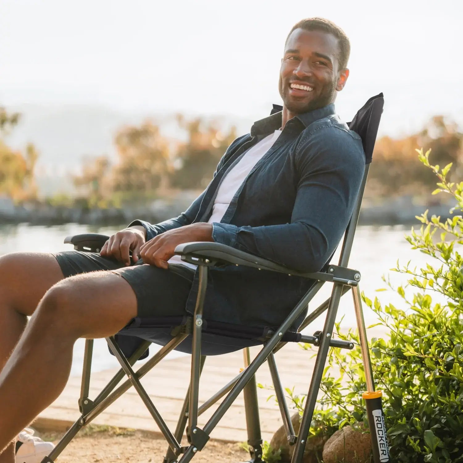 Man sitting comfortably in the indigo RoadTrip Rocker by a lakeside trail.